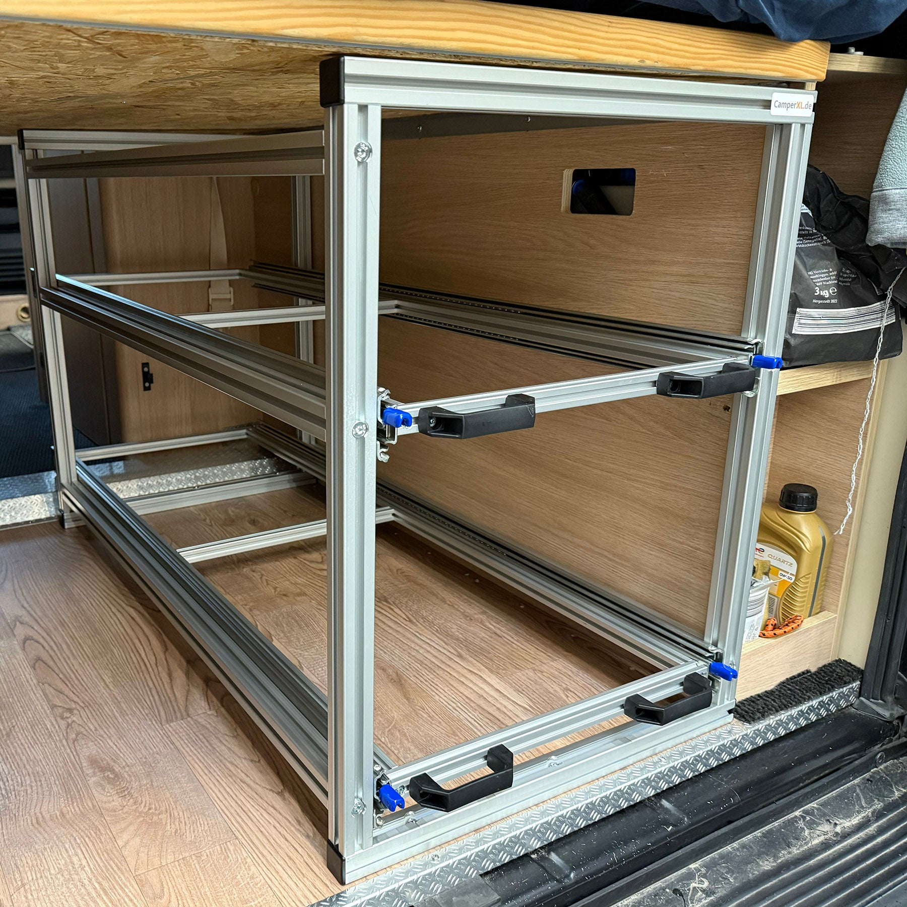 Doppelstöckiger Heckauszug über Versorgungskanal, beladen mit hohen und flachen Euroboxen, getragen von stabilen Aluminiumprofilen.